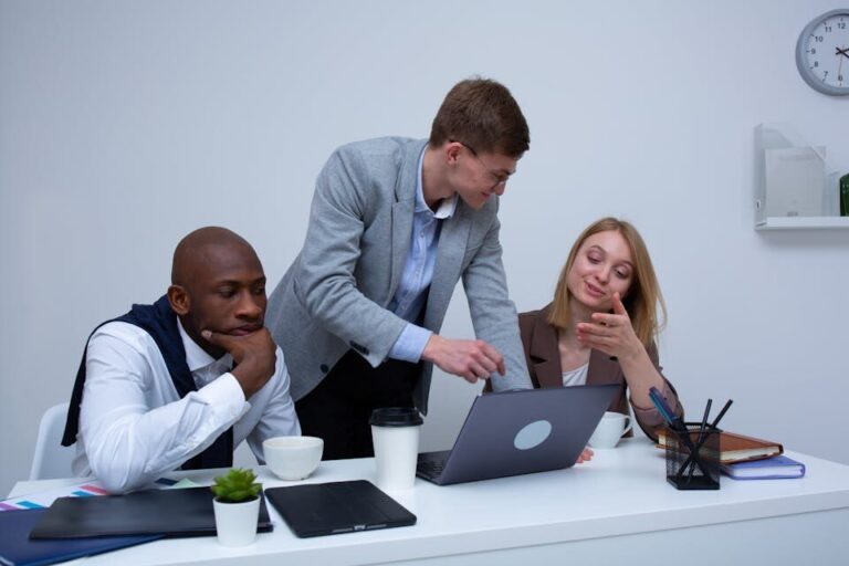 A diverse team collaborating in a modern office environment, discussing work on a laptop.