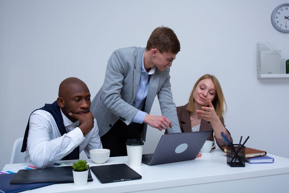 A diverse team collaborating in a modern office environment, discussing work on a laptop.