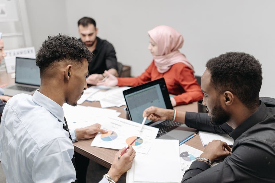 A diverse team collaborating on a project with laptops and documents around a table in an office.