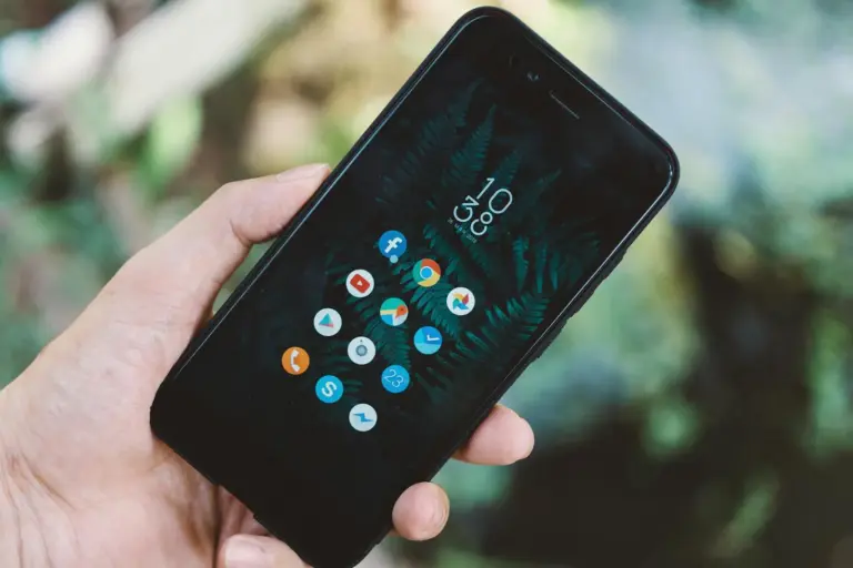 Close-up of a hand holding a smartphone with app icons and a nature wallpaper.